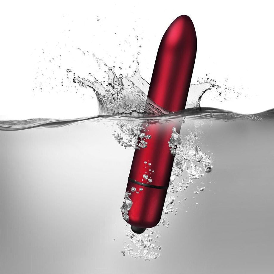 Red electronic massager emerging from water with splashes on a white background