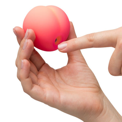 Hand holding a small pink fruit shaped vibe against a white background