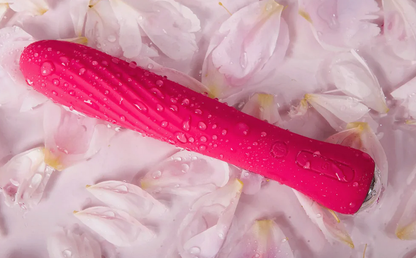 Pink vibrator with water droplets on a bed of pink flowers