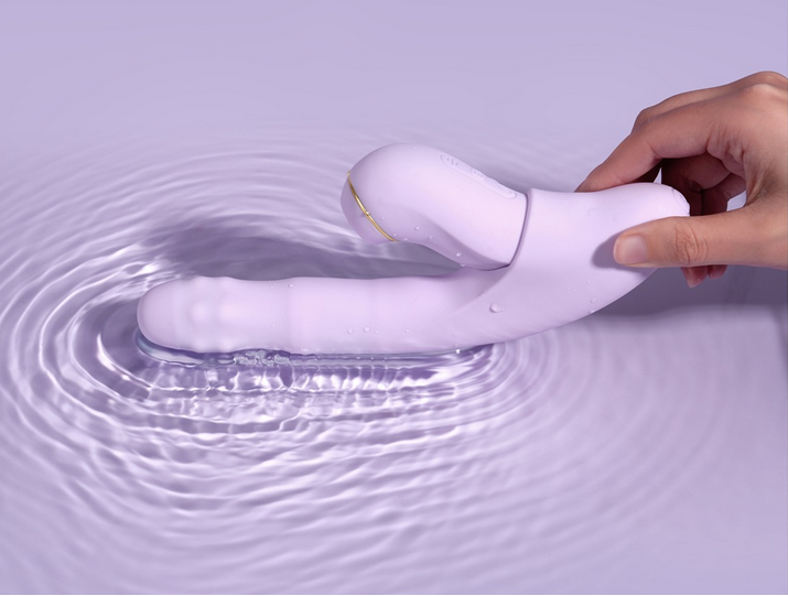 White electronic device being submerged in water with a hand holding it, on a light purple background.