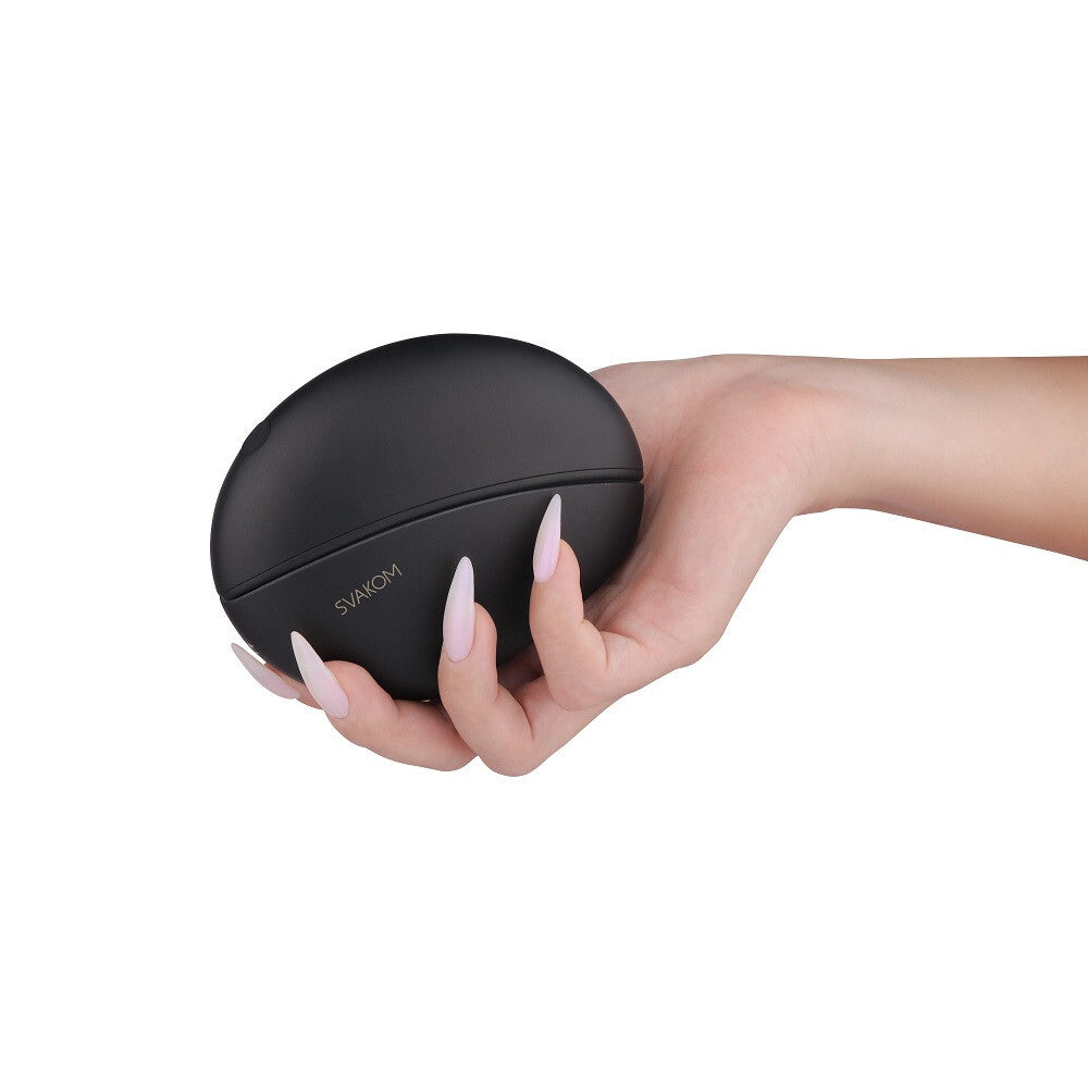 Hand holding a black electronic device with 'SVAKOM' branding on a white background