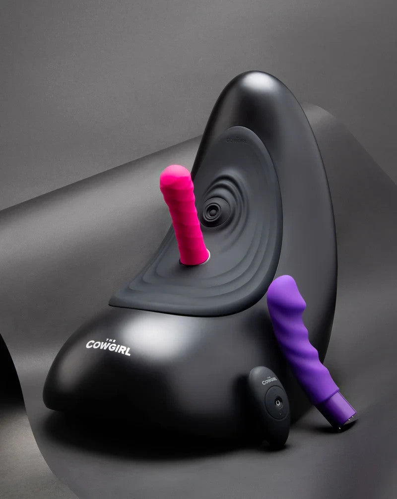 Black sex machine with pink and purple attachments on a gray background