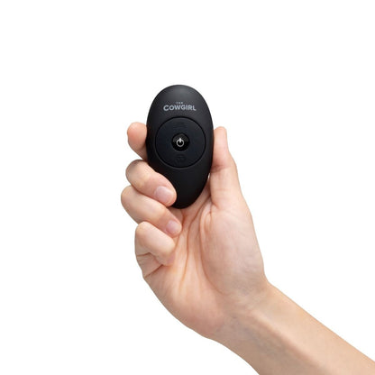 Hand holding a black device with 'The Cowgirl' branding on a white background