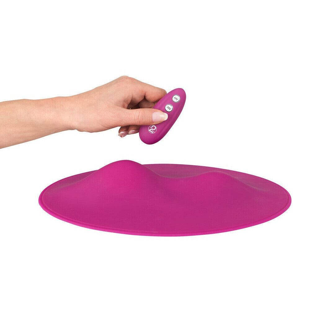 Hand holding a pink electronic vibrator with a large pink mat on a white background