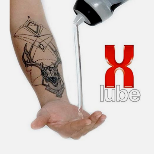 Person applying X-Lube to a tattoo with a pump bottle on a white background