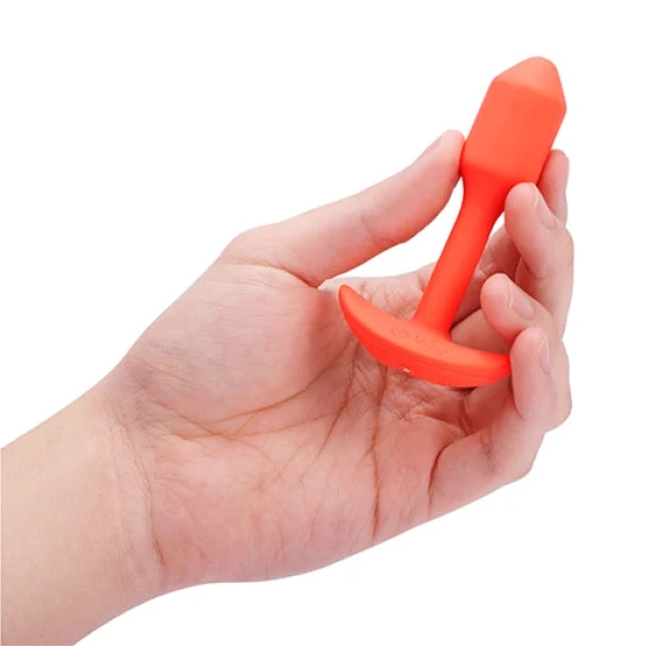 Hand holding a red silicone anchor-shaped anal plug on a white background